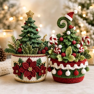 May include: Two crocheted Christmas tree decorations in pots. The left pot is white with red poinsettias and gold beads. The right pot is red and green with white trim and pom-poms. Both trees feature green foliage, red berries, and candy canes.