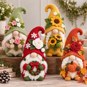 Pode incluir: Quatro figuras de gnomos de crochê com chapéus pontiagudos. Um é verde com flores rosas, um vermelho com uma rosa branca e flocos de neve, um amarelo com girassóis e um laranja com folhas de outono e uma pequena abóbora.