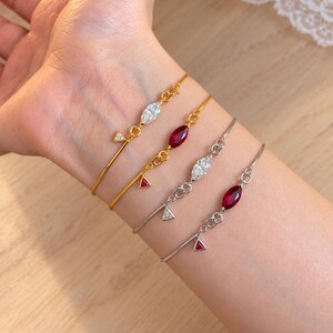 Puede incluir: Cuatro pulseras delicadas con piedras de corte marquesa y pequeños detalles triangulares. Dos pulseras son doradas con piedras transparentes y rojas, y dos son plateadas con piedras transparentes y rojas, todas en cadenas finas.