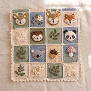 Könnte beinhalten: Eine quadratische Häkeldecke mit einem Raster aus sechzehn Feldern in Salbeigrün, Staubblau und Creme. Die Felder zeigen strukturierte Applikationen von Waldtieren wie Rehen, Füchsen und Pandas sowie botanische Motive wie Blätter, Blumen, eine Eichel und einen Pilz.