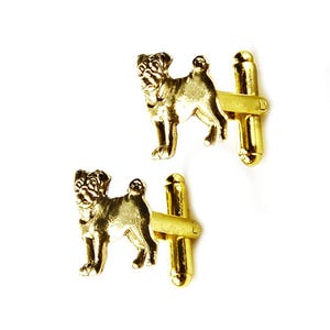 May include: A pair of gold-toned cufflinks featuring a pug dog design. The cufflinks are made of metal and have a polished finish.
