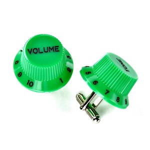 Può includere: Un paio di gemelli verde brillante in stile amplificatore per chitarra. Uno riporta la scritta VOLUME con numeri neri da 1 a 10, l'altro la scritta TONE con numeri neri da 1 a 9. Entrambi presentano bordi laterali zigrinati.