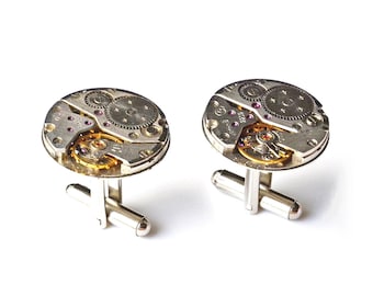 May include: A pair of silver cufflinks with a circular design featuring exposed watch gears and a gold-toned finish.