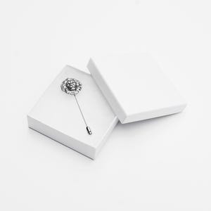Puede incluir: Un broche de solapa de cabeza de le&oacute;n de plata en una caja blanca. El broche est&aacute; en un alfiler de plata y tiene un dise&ntilde;o detallado.