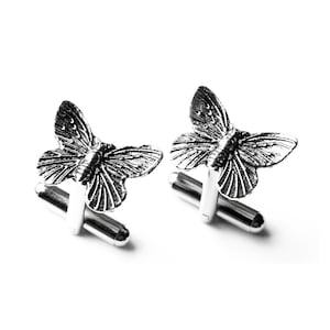 May include: A pair of silver butterfly cufflinks. The butterflies are detailed and have a realistic appearance.