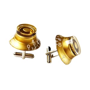 May include: A pair of gold cufflinks shaped like guitar knobs with white numbers. The cufflinks are made of metal and have a clear plastic top.