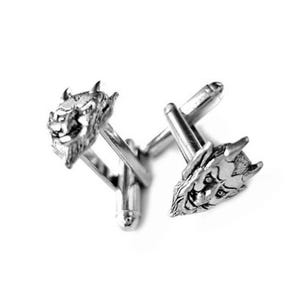 May include: A pair of silver-toned cufflinks featuring detailed dragon head designs. The cufflinks have a classic bar and post closure. The dragon heads are intricately sculpted with horns, facial features, and textured surfaces, creating a striking accessory.