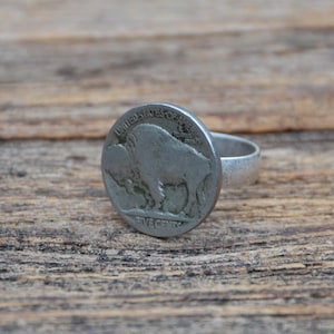 May include: A silver ring featuring a vintage United States five-cent coin. The coin displays a detailed image of a bison. The ring has a simple, smooth band and a circular coin setting.