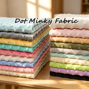 Può includere: Due pile di tessuto Dot Minky piegato in vari colori, tra cui blu, grigio, giallo, verde, rosa, bianco e nero. Ogni pezzo di tessuto presenta un motivo a pois in rilievo sulla superficie. Il testo Dot Minky Fabric è visibile.