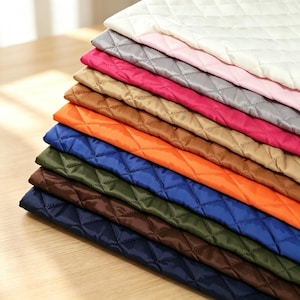 May include: A stack of quilted fabric sheets in various colors including white, light pink, gray, magenta, tan, orange, blue, olive green, brown, and navy blue. Each sheet features a consistent diamond-shaped stitched pattern across the surface.