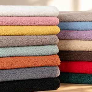 May include: A stack of folded sherpa fabric pieces in various colours including white, pink, yellow, brown, light blue, orange, grey, black, beige, purple, red, and dark green. Each piece features a thick, textured, and fuzzy fleece surface.