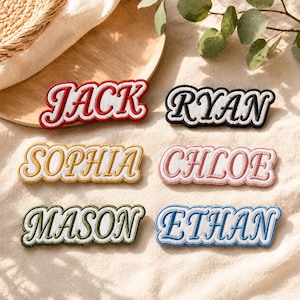 Puede incluir: Seis parches rectangulares bordados con bordes festoneados. Los parches muestran los nombres JACK en rojo, RYAN en negro, SOPHIA en dorado, CHLOE en rosa, MASON en verde y ETHAN en azul. Cada nombre está bordado en una fuente cursiva negrita.