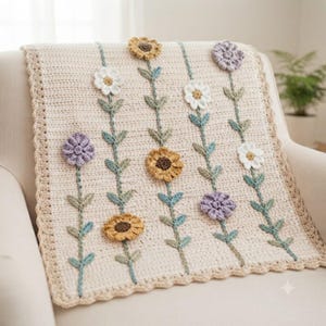 Può includere: Una coperta all'uncinetto color crema con file verticali di fiori applicati nelle tonalità del giallo, bianco e lavanda. Ogni fiore è collegato da steli e foglie verdi all'uncinetto. La coperta presenta un bordo smerlato color marrone chiaro.