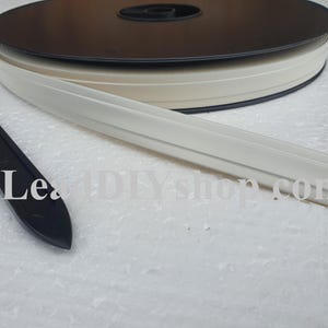 May include: A spool of off-white adhesive trim tape with a central ridge and a black plastic application tool. The text LeadDIYshop.com is visible across the image. The trim is coiled on a black circular reel, featuring a smooth finish.