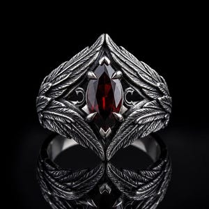 Peut inclure: Une bague en argent avec une pierre précieuse rouge foncé taille marquise maintenue par quatre griffes. L'anneau est orné de motifs de plumes texturés et détaillés qui s'étendent depuis la pierre centrale, créant un aspect symétrique.