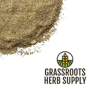 May include: A close-up of a pile of dried, ground herbs. The herbs are a light brown color and have a slightly grainy texture. The image is taken from a high angle, and the herbs are spread out in a shallow pile. The background is white.