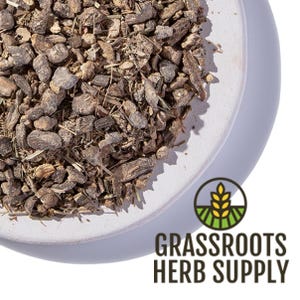 May include: A close-up of dried, brown, and grey roots and herbs in a white ceramic bowl. The bowl is on a white surface. The text "GRASSROOTS HERB SUPPLY" is in the lower right corner of the image.