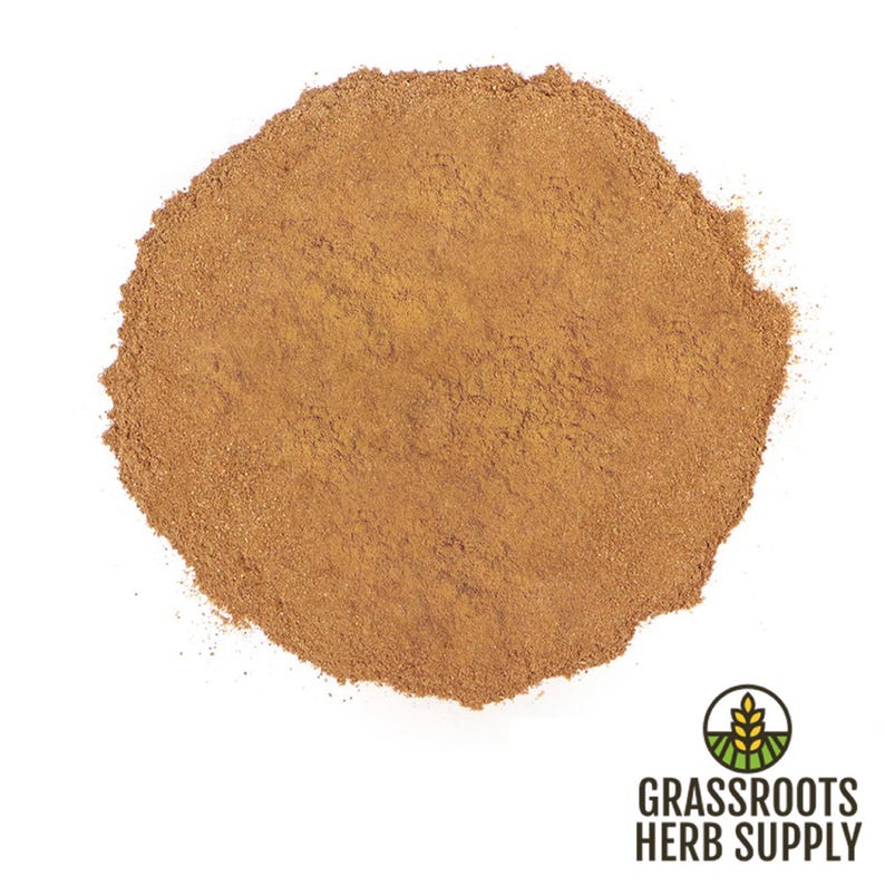 May include: A close-up view of a pile of ground cinnamon, a warm brown spice, on a white background. The cinnamon is finely ground and has a smooth texture.