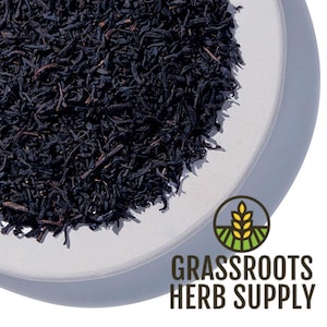 May include: Close-up of loose-leaf black tea on a white plate. The tea leaves are dark brown and appear dry. The image includes the text "GRASSROOTS HERB SUPPLY" with a logo of a wheat stalk.