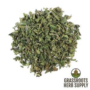 May include: Dried nettle leaves, a green herbal ingredient, in a loose pile on a white background. The image is labeled "Grassroots Herb Supply".