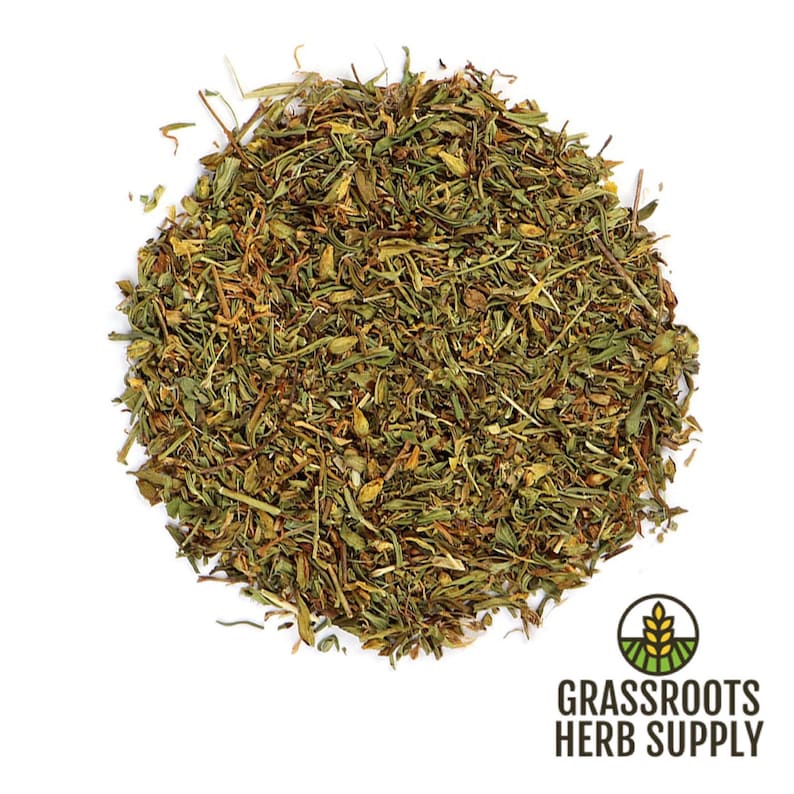 May include: A close-up of a pile of dried, green and brown herbs. The herbs are loose and scattered on a white background. The text "GRASSROOTS HERB SUPPLY" is visible in the lower right corner of the image.