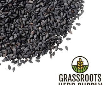 May include: A close-up view of a pile of black sesame seeds. The seeds are small and oval-shaped, with a slightly rough texture. The seeds are a deep black color and are scattered across a white background.