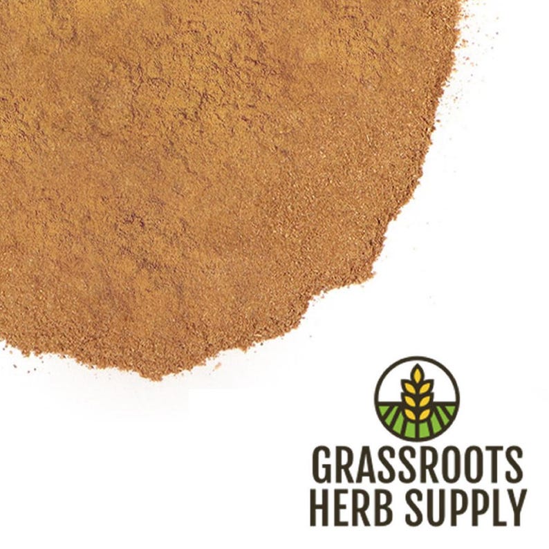 May include: A close-up of a pile of ground cinnamon powder. The powder is a light brown color and has a fine texture. The powder is piled on a white surface.