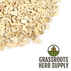 Op de afbeelding: Close-up van een stapel gehakte, gedroogde kruiden, met een lichtbeige kleur. De kruiden zijn onregelmatig van vorm en textuur. De afbeelding bevat het logo van Grassroots Herb Supply, een cirkelvormig ontwerp met een tarwe-aar.