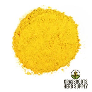 May include: A close-up of a pile of bright yellow turmeric powder on a white background. The powder is finely ground and has a smooth texture.