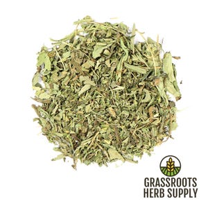 May include: A pile of dried stevia leaves, a natural sweetener, on a white background. The leaves are a light green color and have a slightly rough texture. The image is taken from a top-down perspective.  Grassroots Herb Supply is printed in brown text on a green and yellow logo.