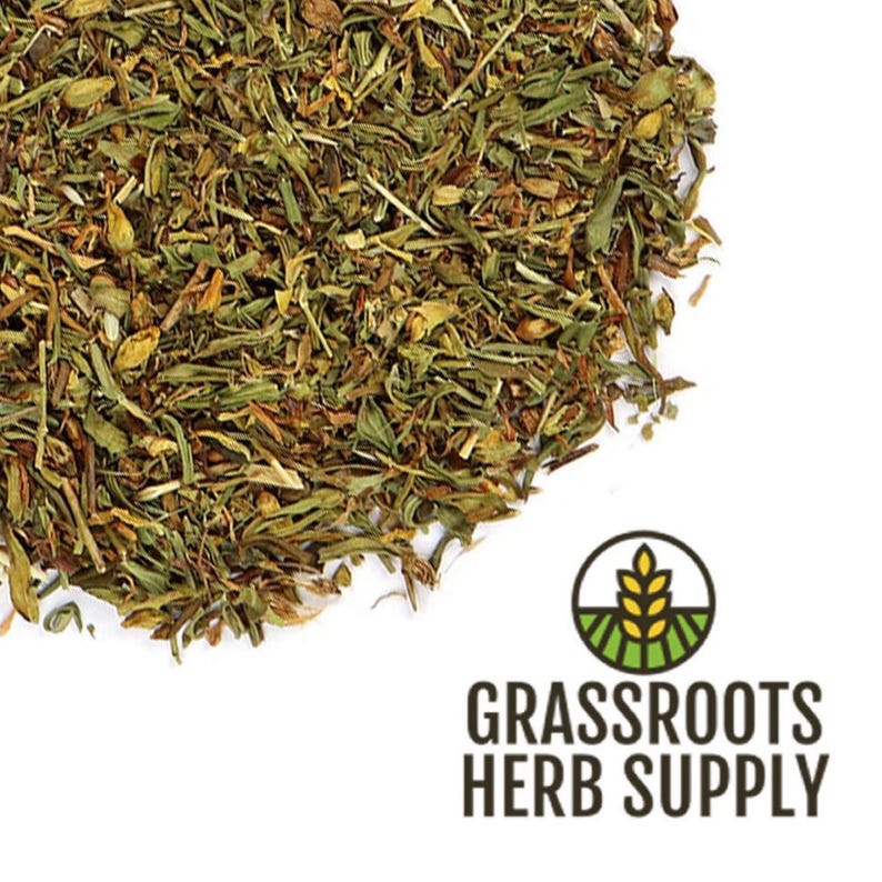 May include: A close-up of dried green and brown herbs, likely a blend of various herbs. The herbs are scattered on a white surface. The image includes the text "GRASSROOTS HERB SUPPLY".