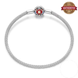 May include: A silver mesh bracelet featuring a circular clasp with a red enamel center, a small yellow stone, and tiny blue and orange accents. The clasp has an intricate, swirling metal design and connects to a flexible, woven silver chain.