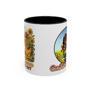 May include: A white ceramic mug with a black interior and rim, featuring a cartoon illustration of chickens in a sunflower field with the text FUCK AROUND AND FIND OUT, and a circular graphic of a person in a sunflower field with the text Canna.