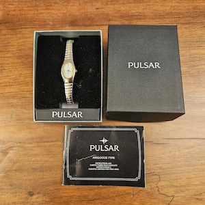 Peut inclure: Une montre analogique Pulsar avec un bracelet extensible en métal argenté et doré et un cadran rond blanc, présentée dans une boîte noire de la marque avec un manuel d'instructions assorti portant le texte Pulsar Analogue Type.