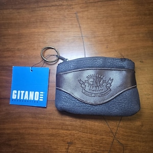 May include: A dark blue textured coin purse with a brown leather-like horizontal band featuring an embossed Gitano New York logo. A metal key ring is attached to the top zipper. A square blue tag with the white text Gitano Accessories is attached.