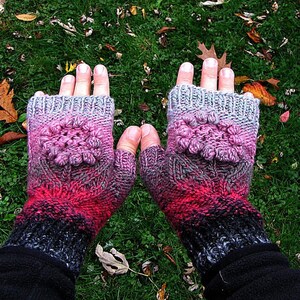 May include: A pair of fingerless gloves with a pink floral design. The gloves are knit in a gradient of black, gray, pink, and red.