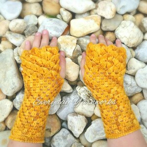 May include: A pair of yellow crocheted fingerless gloves with a textured pattern. The gloves are on a background of small, smooth stones.