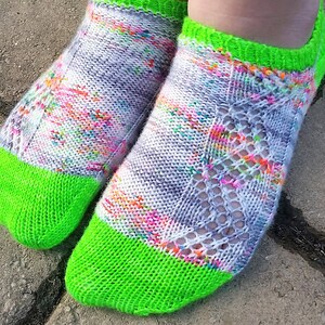 May include: A pair of colorful knit socks with a white base and a bright green toe and cuff. The socks have a lacy pattern.