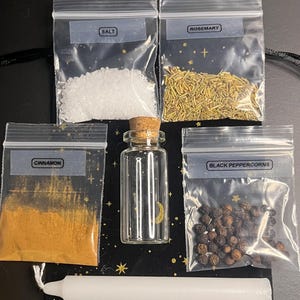 以下が含まれることがあります： 塩、ローズマリー、シナモン、黒胡椒が入った4つの透明なプラスチック袋と、それぞれのラベル。コルク栓付きの小さなガラス瓶と白いテーパーキャンドルが、星柄の黒い布製ポーチの上に配置されています。