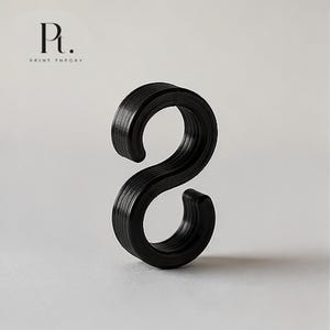 May include: A black, S-shaped hook with a layered, ribbed texture on its surface. The object features a curved top and bottom section, creating a continuous, rounded form. The logo Pt. PRINT THEORY is visible in the upper left corner of the image.