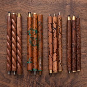 May include: Twelve cylindrical wooden walking stick segments arranged in four groups of three. The set includes three smooth twisted shafts, three with green fractal patterns, three with dark lightning-like markings, and three with intricate floral carvings.