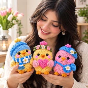 May include: Three small, round, crocheted bird figures. The left bird is yellow with a blue hat and scarf. The centre bird is yellow with a floral crown and a pink heart. The right bird is pink with a blue hat and a small blue bag.