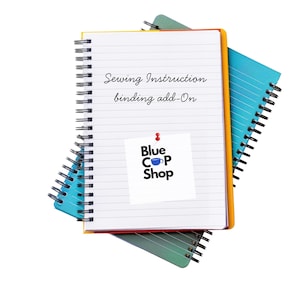 May include: A stack of three spiral-bound notebooks. The top notebook is open, displaying the text "Sewing Instruction binding add-On" and a sticker with the "Blue Cop Shop" logo. The notebooks are in yellow, blue, and green.
