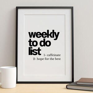 May include: A framed print with the words "weekly to do list" in bold black font. The list includes "1- caffeinate" and "2- hope for the best." A white mug, a closed book, and a pencil are on the table.