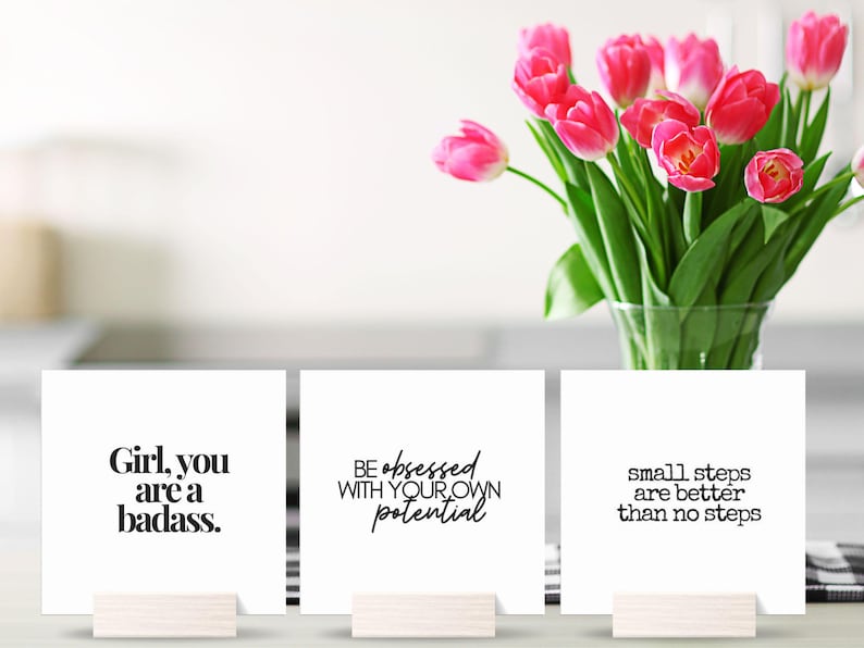 May include: Three white cards with inspirational quotes printed in black. The quotes are "Girl, you are a badass.", "Be obsessed with your own potential", and "Small steps are better than no steps".