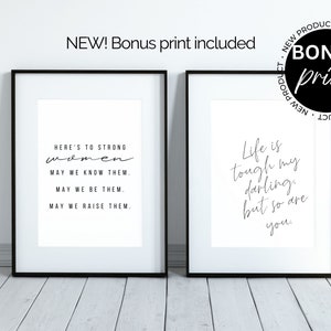 May include: Two black framed prints with white backgrounds and black text. The left print reads "Here's to strong women. May we know them. May we be them. May we raise them." The right print reads "Life is tough my darling, but so are you."