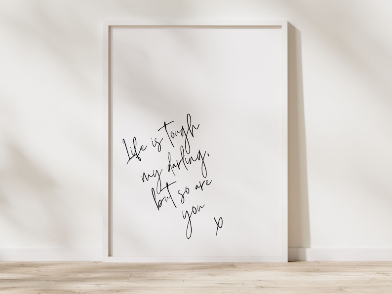 May include: A white framed print with black calligraphy that reads "Life is tough, my darlings, but so are you."