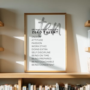 May include: A framed print with the words "ten things that require ZERO TALENT" in a modern font. The list includes "Energy, Attitude, Passion, Work Ethic" and more. The print is displayed on a wooden shelf surrounded by books.