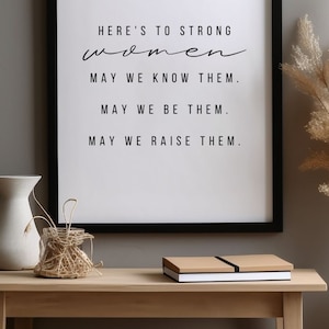 May include: Black framed print with the text "HERE'S TO STRONG women MAY WE KNOW THEM. MAY WE BE THEM. MAY WE RAISE THEM."