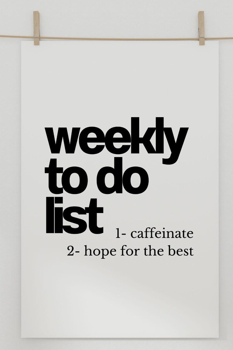 May include: A white poster with the words "weekly to do list" in bold black font. Below, the list includes "1- caffeinate" and "2- hope for the best." The poster is held by two wooden clothes pegs.